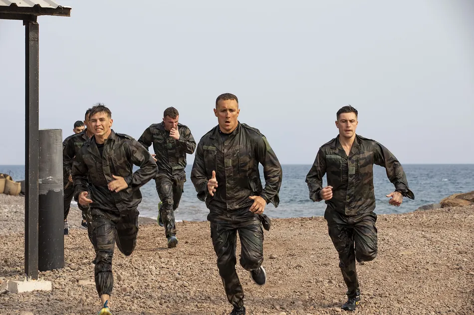 Un groupe de candidats court en tenue camouflée le long du littoral