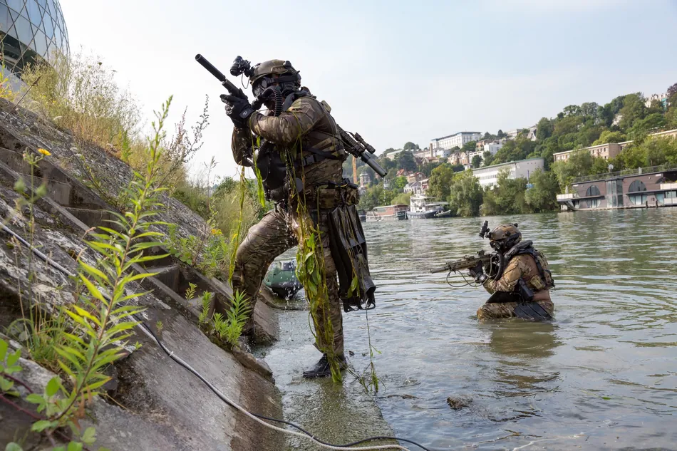 Des militaires progressent en tenue complète dans l'eau, matériel porté